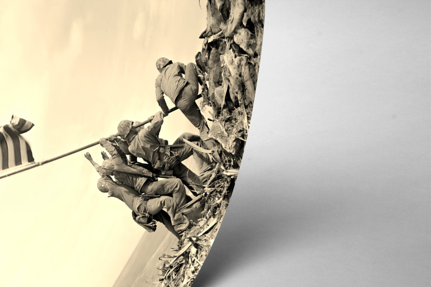 A black and white image depicting a group of soldiers working together to pull up a flag on a rocky hill, with a flagpole visible in the foreground.