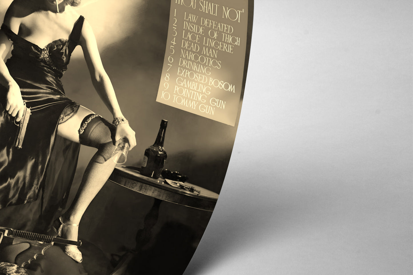 The image is a black and white photograph of a woman in a revealing outfit, holding a gun and standing next to a table with a bottle of alcohol.