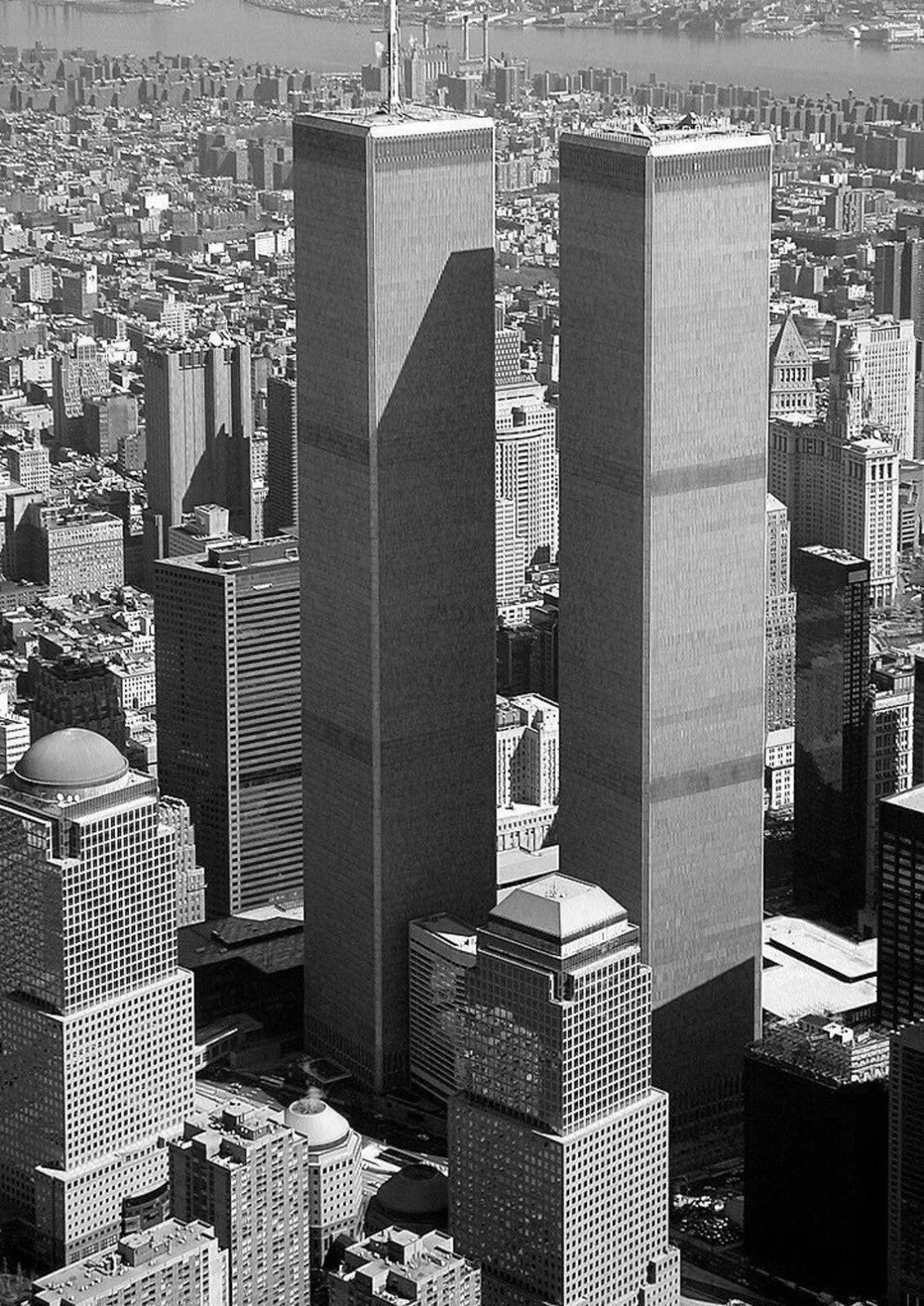 A black and white aerial view of a densely populated city with numerous skyscrapers and buildings, including two prominent twin towers.
