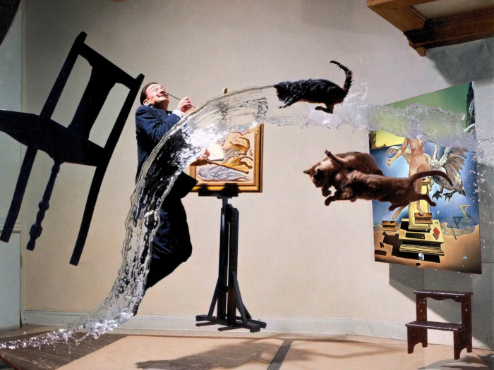 A man in a suit is painting a picture in a room filled with water, with two cats jumping out of the water onto the painting.