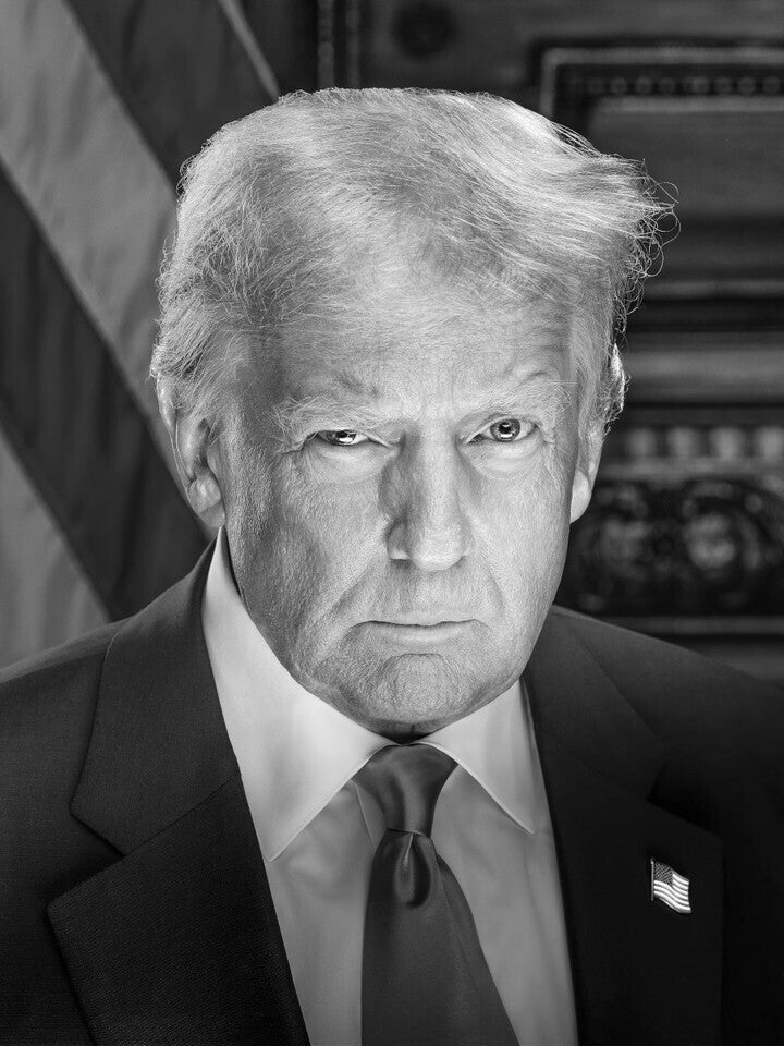 A black and white portrait of a man wearing a suit and tie, with an American flag in the background.