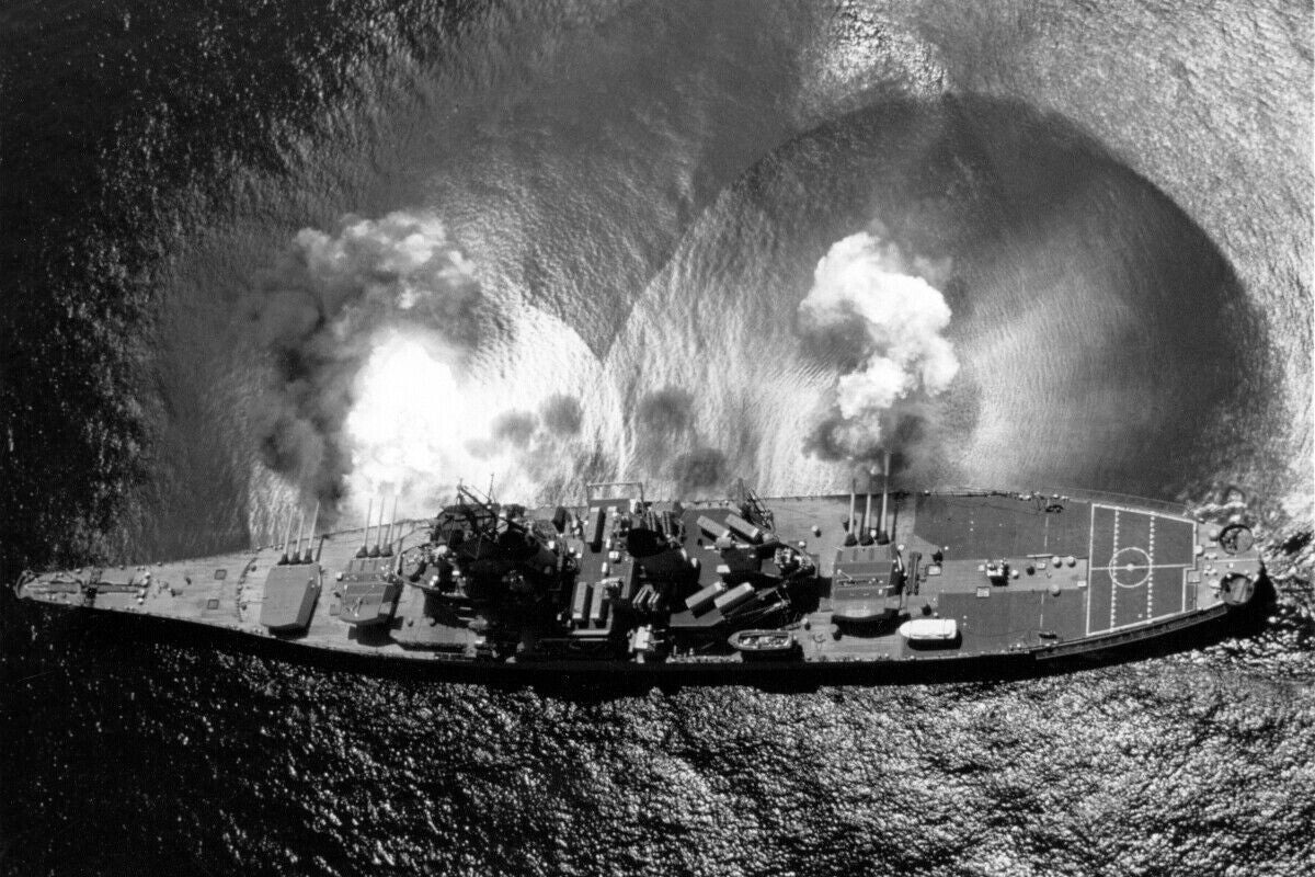 A large naval ship with multiple decks and various equipment is shown sailing on the water, with smoke billowing from its cannons.