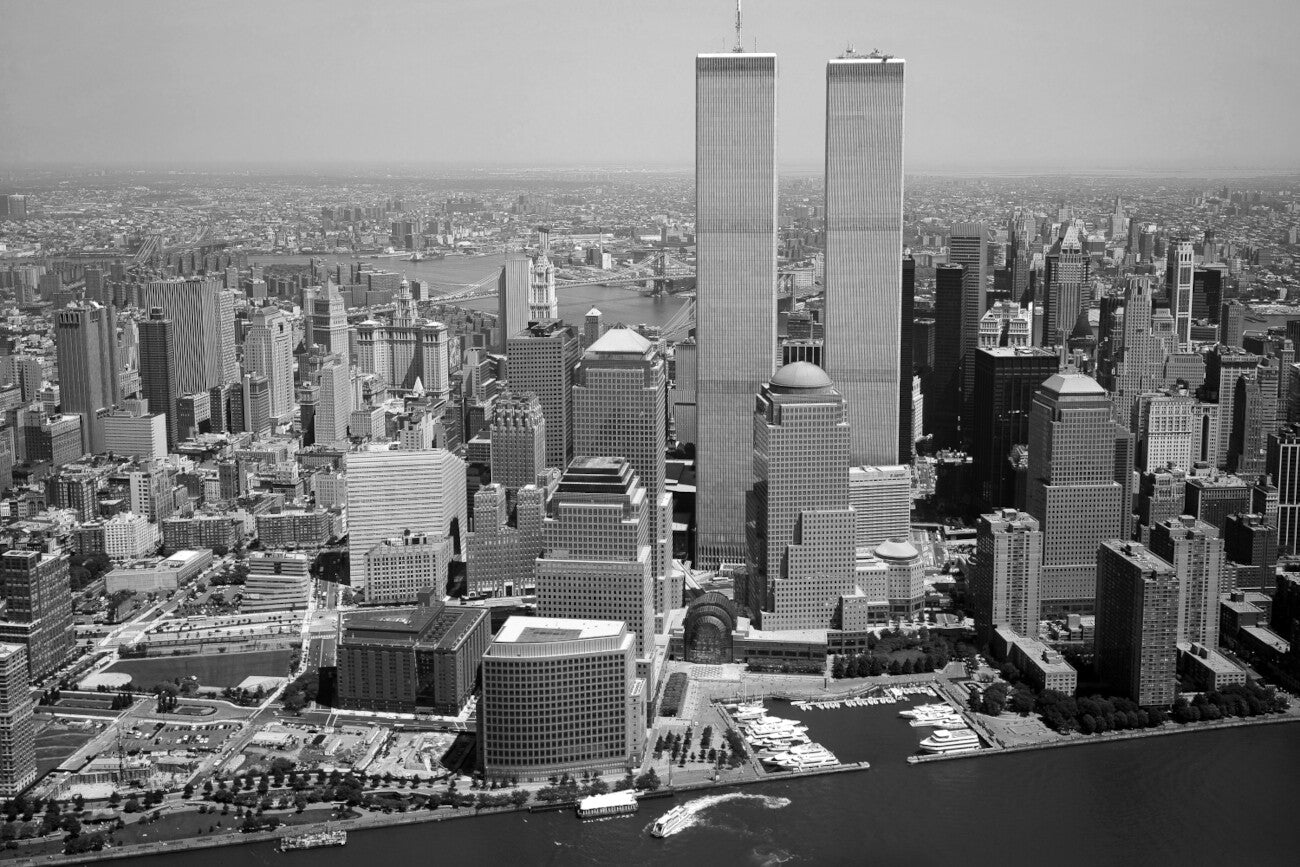 The image is a black and white aerial view of the New York City skyline, featuring the iconic twin towers of the World Trade Center.