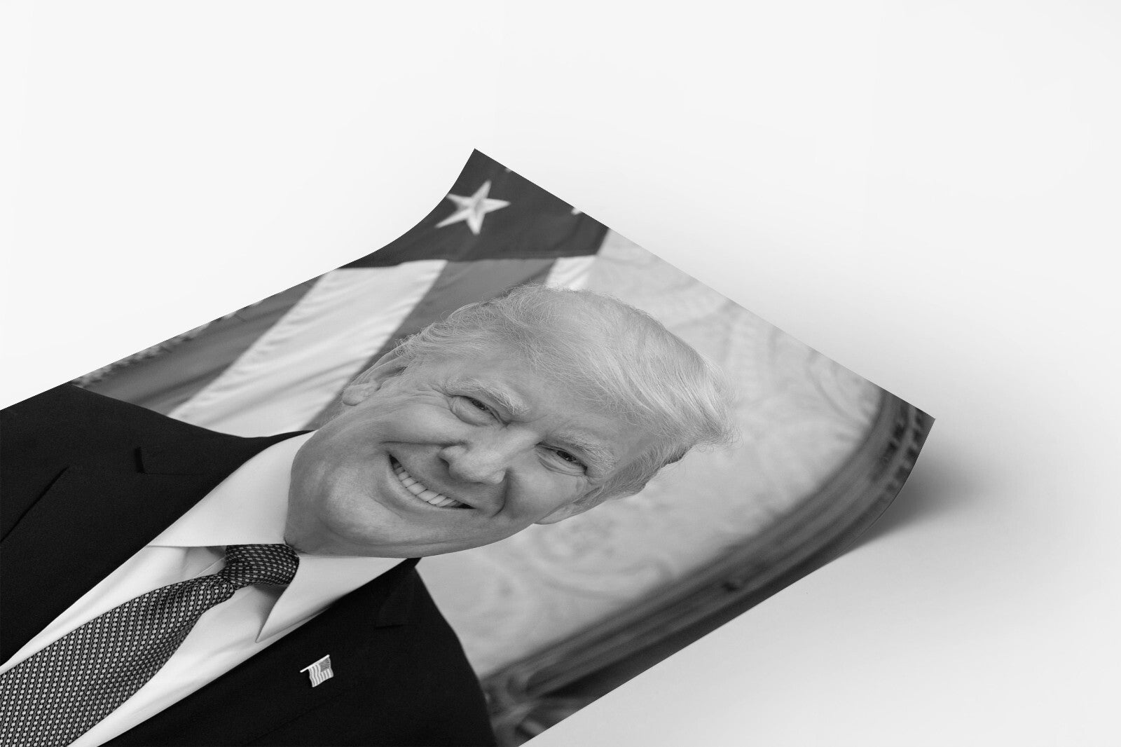 A black and white photograph of a smiling man wearing a suit and tie, with an American flag in the background.