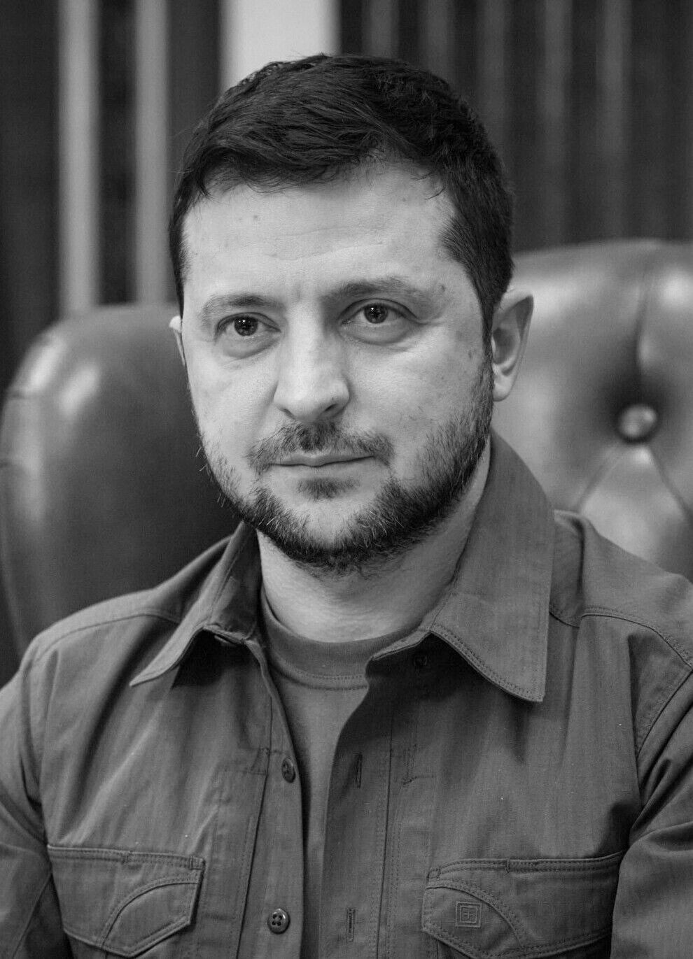 A black and white portrait of a man with a beard, wearing a collared shirt, sitting in a chair.