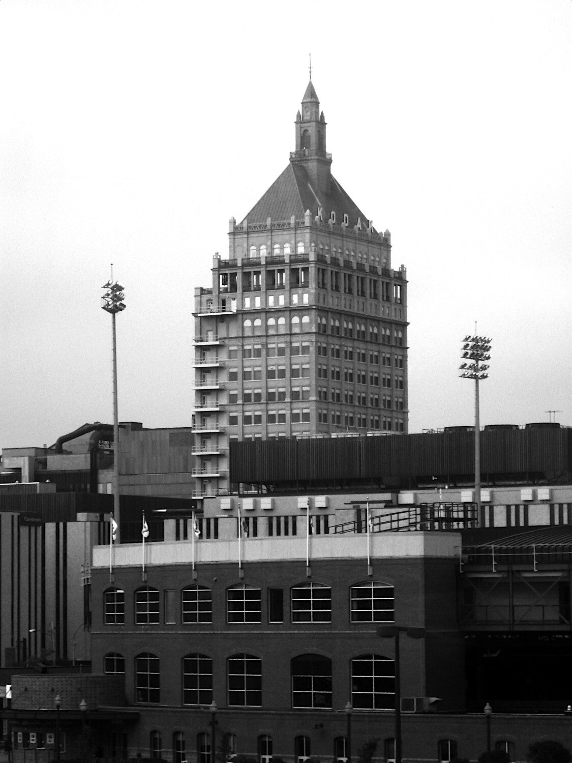 A black and white image of a tall, ornate building with a pointed roof and multiple levels, surrounded by other buildings and structures.