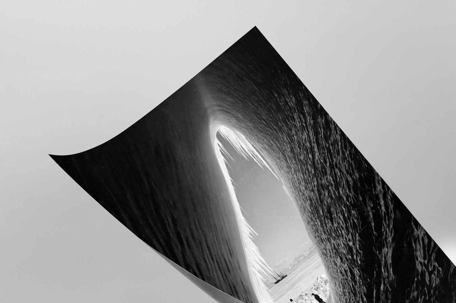 A black and white image depicting a curved, textured surface with a small opening or archway, creating a sense of depth and perspective.