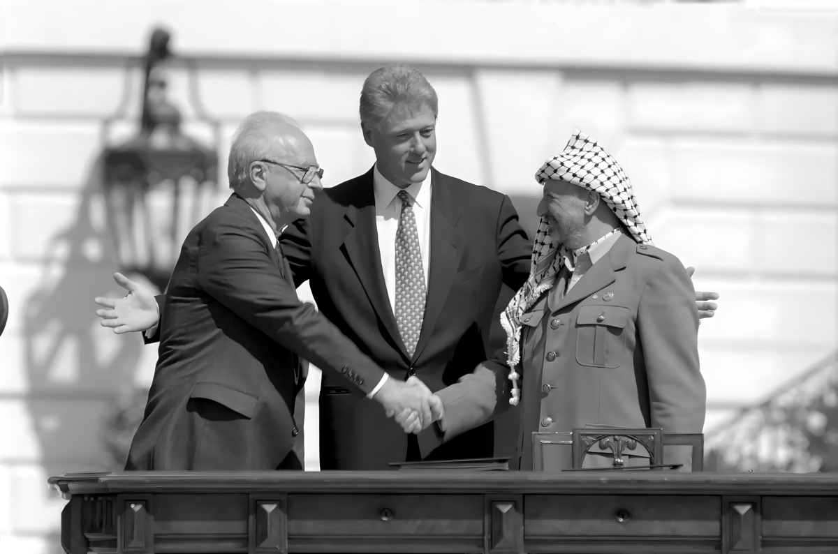 A black and white photograph showing three men shaking hands, with one man wearing a suit and tie and the other two wearing military uniforms.